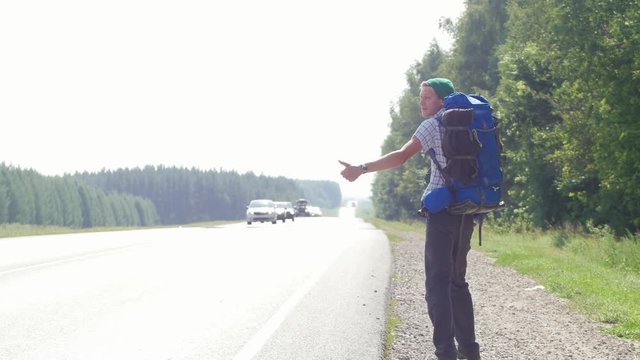 A young man with a big backpack honking and goes along the road from the camera