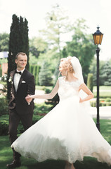 Stylish couple of happy newlyweds walking in the park on their wedding day with bouquet