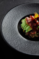 close-up view of delicious traditional japanese dish with seafood, avocado and herbs on black plate