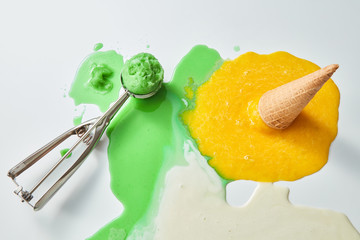 Green and yellow melting ice cream with waffle cone and scoop on white background. Summer concept....