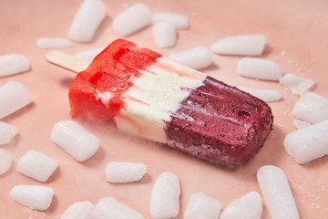 Frozen berry smoothies. Multicolored ice cream on a stick with slices of ice on a pink background