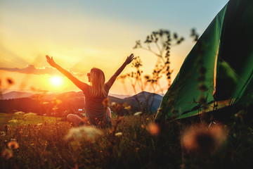 Happy woman with open arms stay near tent around mountains under sun