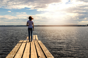 Fototapeta premium A girl is standing on a wooden pier on the background of the sea