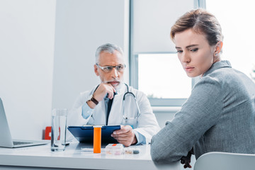 sad female patient looking away while mature male doctor sitting near at table in office