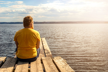 Fototapeta premium A man sits on a wooden pier and looks at the sea
