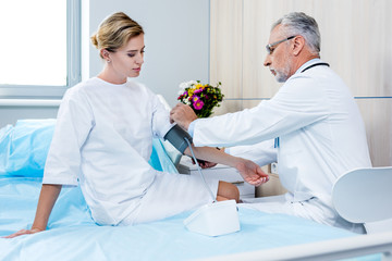 Fototapeta premium side view of middle aged male doctor putting on device for measuring pressure on female patient hand in hospital room