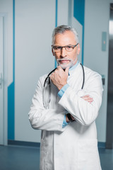 thoughtful middle aged male doctor with stethoscope over neck looking at camera in hospital