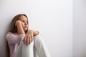 Pensive young teenager girl sitting by the wall on the floor