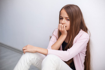 Worried young teenager girl sitting on the floor by the wall - medium portrait