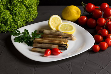 Fresh seafood with parsley and lemon, salad and tomatoes, italian cuisine, mediterranean food on a white plate, grey backgraund