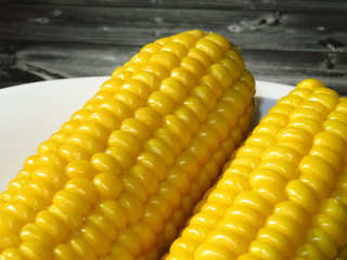 Boiled sweet corn cobs sprinkled with salt. Ready to eat corn on white plate and wooden table, close-up