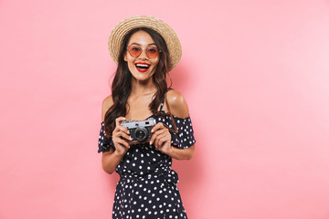 Woman photographer isolated over pink background holding camera.