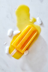 Yellow Icecream lolly pop over marble light background with ice and juice, flat lay
