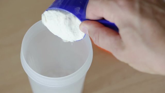The man pours out the protein powder into the glass shaker.