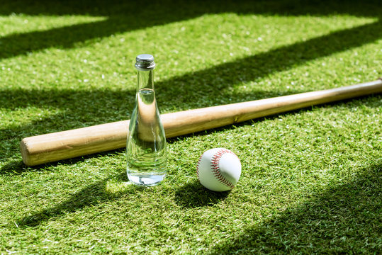 glass water battle with baseball ball and bat lying on green grass