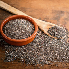 Chia seeds in a clay bowl and  wooden spoon on wood background.   Copy space..
