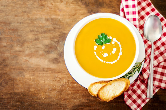 Bowl of vegetable yellow soup with parsley and croutons over wooden background.  Autumn Pumpkin and carrot soup with cream. Copy space.