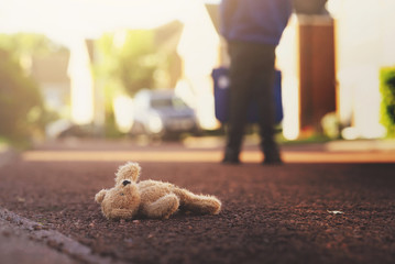 Teddy bear laying on the road with blurry background of school kid carrying school bag,Lonely brown...