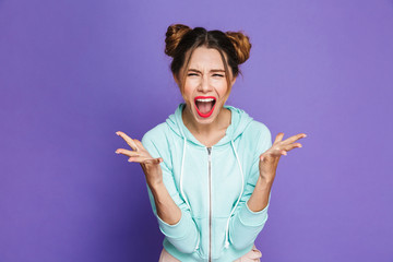 Portrait of angry woman with two buns yelling and throwing up hands, isolated over violet...