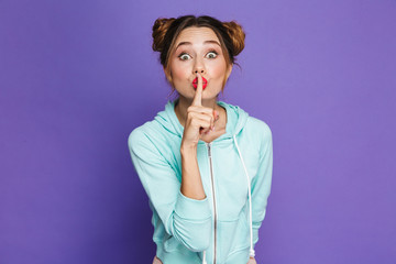 Portrait of caucasian woman with two buns holding index finger on lips and asking to keep silence,...