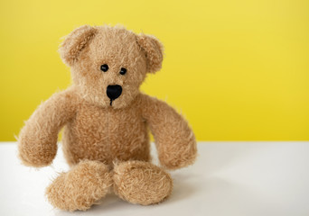 Portrait of teddy bear sitting alone on white table with yellow background, One brown bear toy with with copy space
