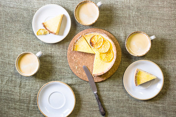 Lemon tart on the table among saucers and cups of coffee. Homemade pastries and homemade cosiness. Top view, flat lay
