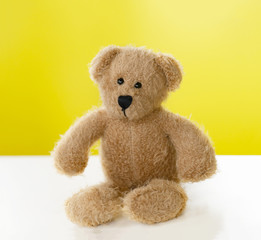 Portrait of teddy bear sitting alone on white table with yellow background, One brown bear toy with with copy space