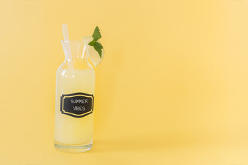 Lemonade jar, overwritten summer vibes, with mint and a slice of lime and pipette on yellow color background and with writing space