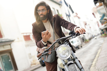 Obraz na płótnie Canvas Hipster guy with electric vintage style bike using smartphone
