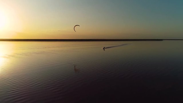 Couple stands in the middle of the estuary and watches as the person is engaged in kitesurfing at sunset
