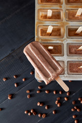 Homemade popsicles with chocolate on ice cube container with coffee beans on dark wooden background, flat lay. Homemade prepare concept