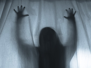 Screaming human pressing through fabric curtain as horror background . Trapped in shadows