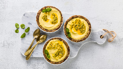 banner of vegan raw mini tarts from nuts and dates with cashew cream from mango purée with lime juice and seeds of passion fruit. healthy alternative food on a white marble board