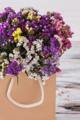 Multicolored flowers in paper package. Close up. White wooden background.