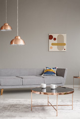 Copper table and lamps in a grey living room interior. Real photo
