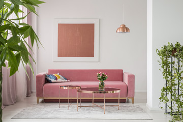 Real photo of a pink couch, round coffee tables and painting in a modern living room interior