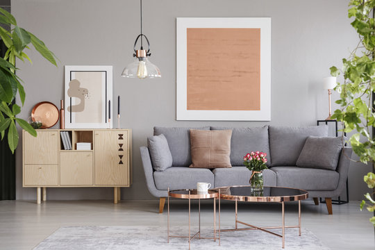 Real photo of a wooden cupboard next to a sofa in a modern living room interior with a big painting