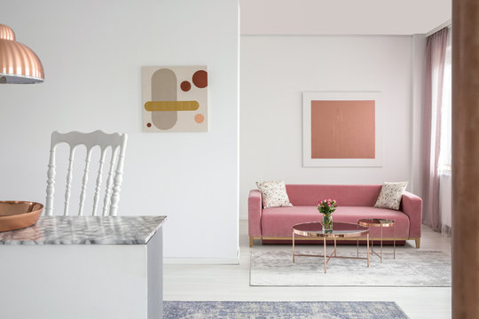 Real photo of paintings in a spacious living room interior with a pink sofa and copper coffee table