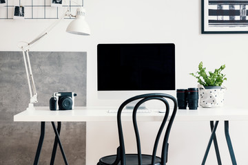 Black chair by a white desk with a computer and a lamp in a modern home office interior for a professional photographer freelancer. Real photo.