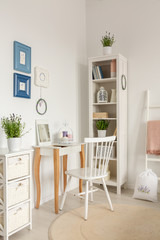 White chair at dressing table next to cabinet with plant in bedroom interior with posters. Real photo