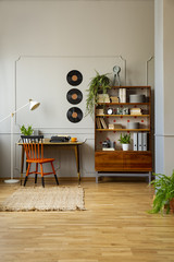Orange chair at desk in grey freelancer's interior with vinyl next to wooden cabinet. Real photo