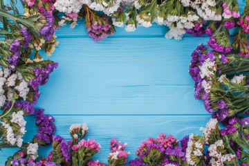 Multicolored dried statice flowers arranged around. Free space for your text, copyspace. Blue wooden table background.