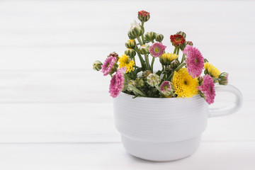 Unripe flowers in a white mug. White wooden table background.