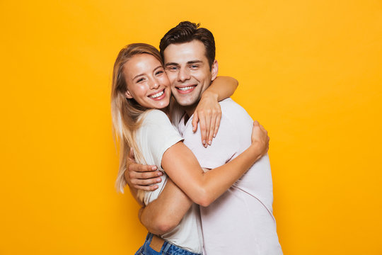 Loving couple standing isolated over yellow wall background hugging.