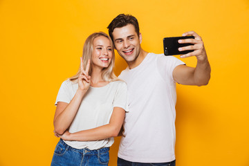 Naklejka premium Young loving couple standing isolated over yellow wall background take a selfie by mobile phone.
