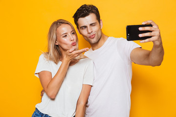 Young loving couple standing isolated over yellow wall background take a selfie by mobile phone.