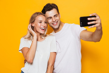 Young loving couple standing isolated over yellow wall background take a selfie by mobile phone.