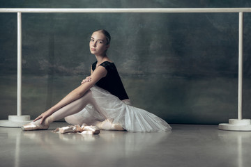 The classic ballet dancer in white tutu posing at ballet barre on studio background. Young teen...