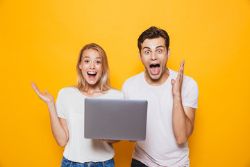Happy excited young loving couple isolated over yellow wall background using laptop computer. - Powered by Adobe