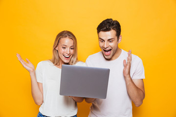 Happy excited young loving couple isolated over yellow wall background using laptop computer.